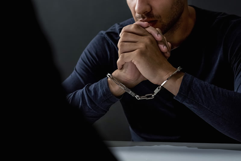 Handcuffed man sitting at a desk with a silhouette of someone in front of him